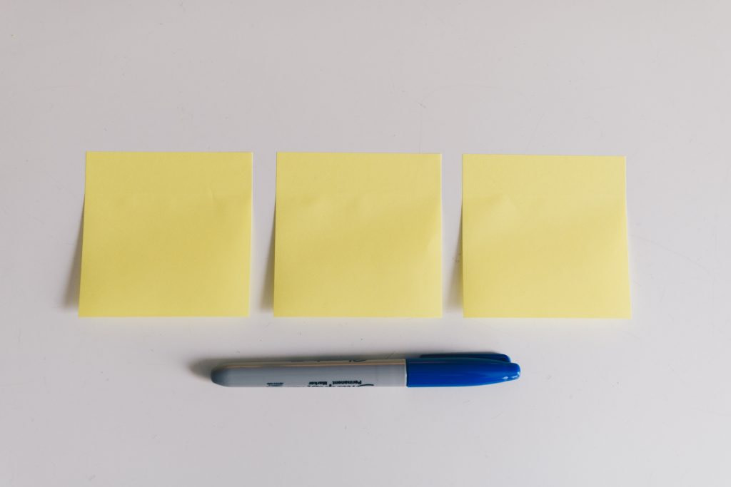 three yellow post-it notes in a row on a white background with a blue-capped sharpie lying beneath it