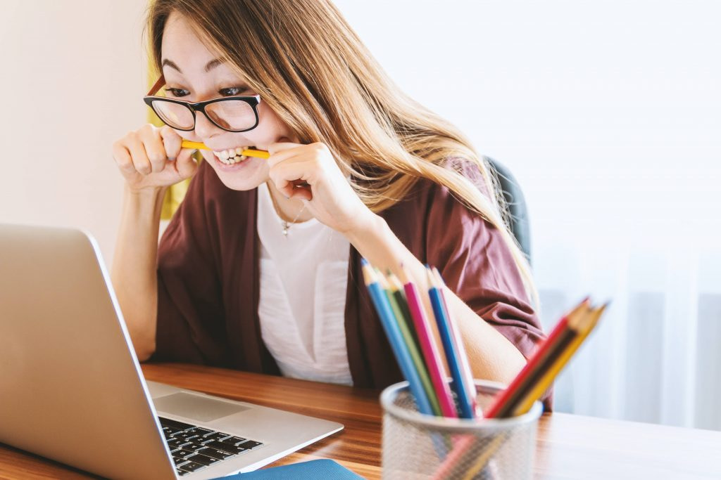 Woman wearing glasses biting on a pencil sitting in front of a laptop at desk