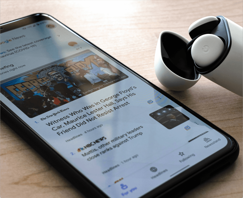 smart phone on a table portraying a news feed with a sed of airpods in its container next to it 